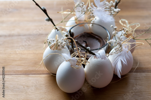  Oster und Frühlingsdeko mit einer Kerze, weiße Eier im Kreis schön mit Naturmaterialien dekoriert auf einem Holztisch. Kätzchen Federn und Co. photo