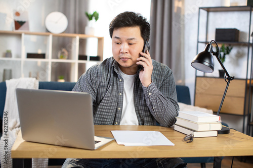 Asian businessman talking on mobile and working on laptop