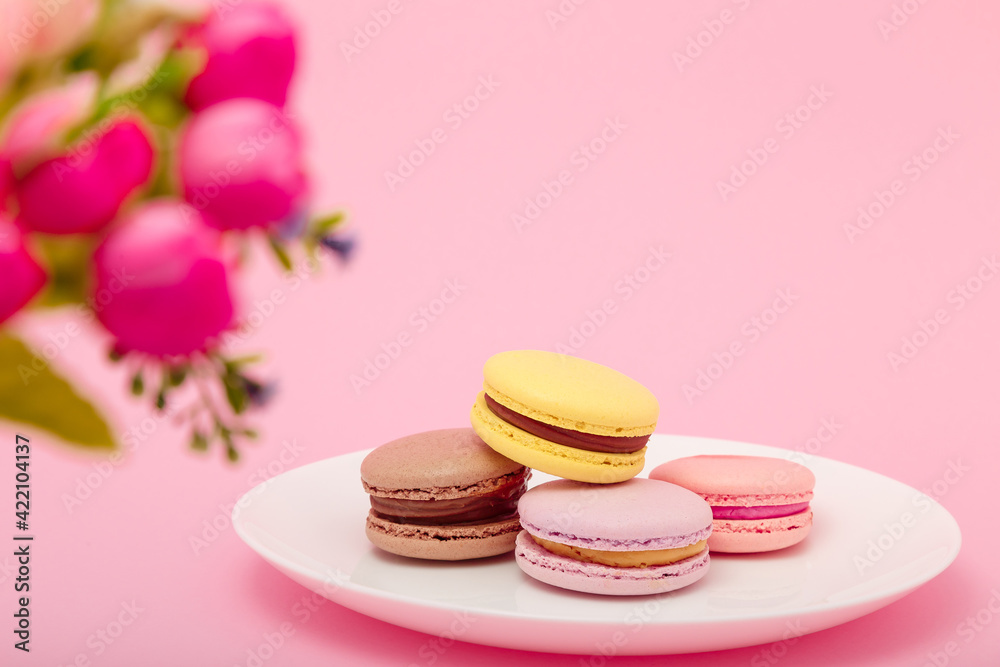 Plate of macaroons on pink background with flowers. Sweet pastry, baked products, sweets, dessert. Unhealthy diet, sugar dependence. Plate of macaroons on pink background with flowers. Sweet pastry, baked products, sweets, dessert. Unhealthy diet, sugar dependence.