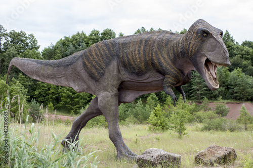 A model of a prehistoric dinosaur made available to visitors to a Jurassic park to learn about the history of many millions of years. In the background  vegetation and terrain resembling the natural h