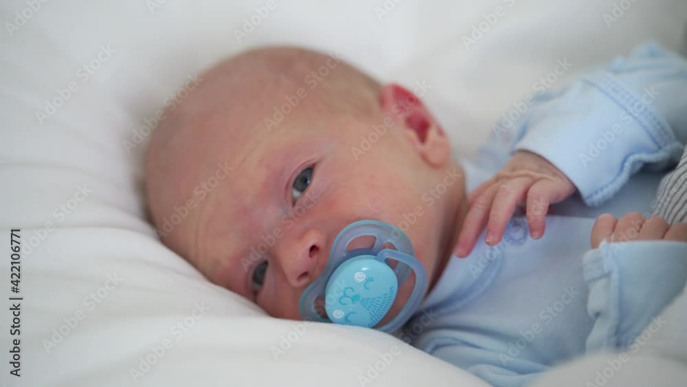 Infant boy lying in crib on white bedspread, newborn baby sucking nipple, face of three week old baby boy closeup Infant boy lying in crib on white bedspread, newborn baby sucking nipple, face of three week old baby boy closeup
