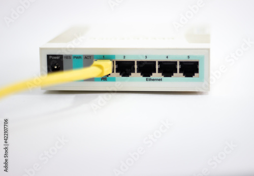 Network cable is plugged into router. Yellow cable in Wi-Fi router. White router with power cord. Router rear view with connections.
