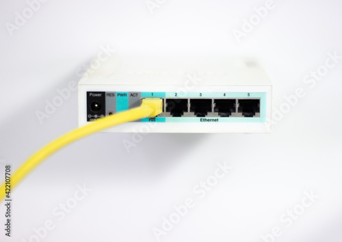 Network cable is plugged into router. Yellow cable in Wi-Fi router. White router with power cord. Router rear view with connections.