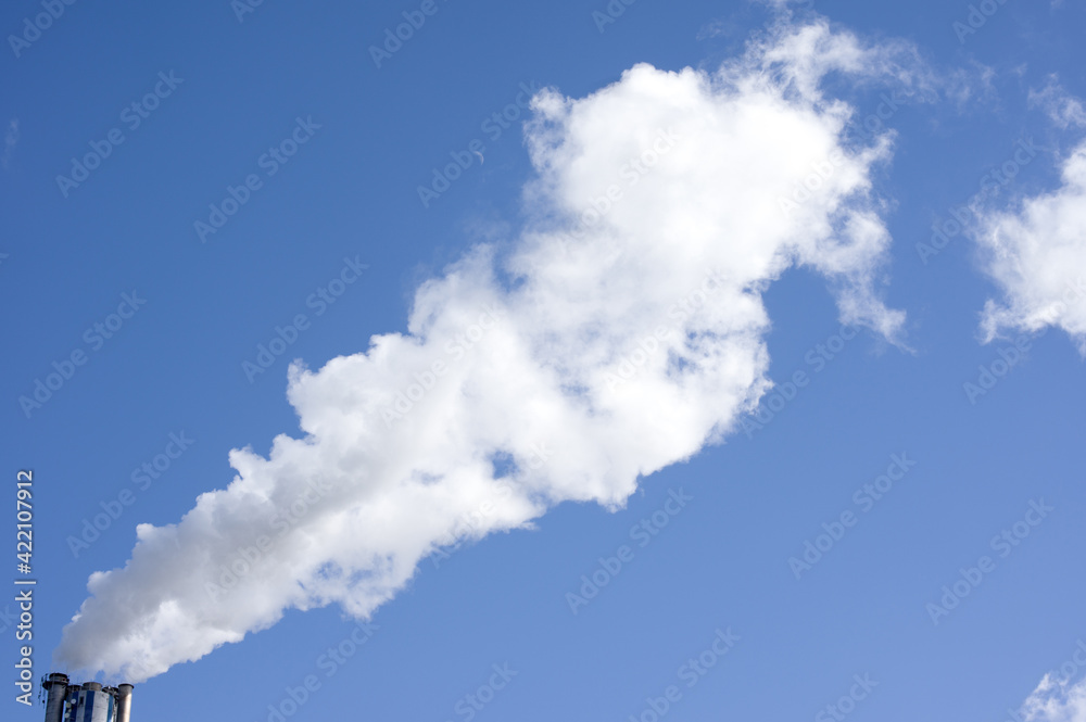 Industrial chimney with a large plume of smoke and a clear blue sky