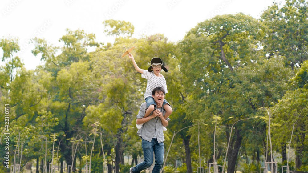 Lifestyle Asian family Father and son sat on his shoulders and run in  park. Paper plane as a toy in hand of kid And there are many big trees in garden Is natural in the morning of summer