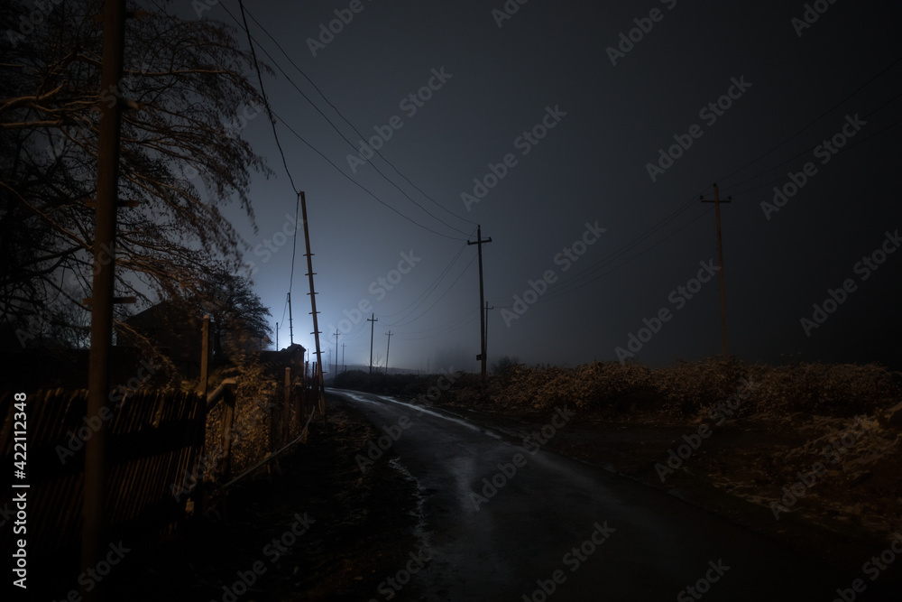 Night street country road with buildings and fences covered in fog lamp . Or Mysterious night in Azerbaijan mountain village