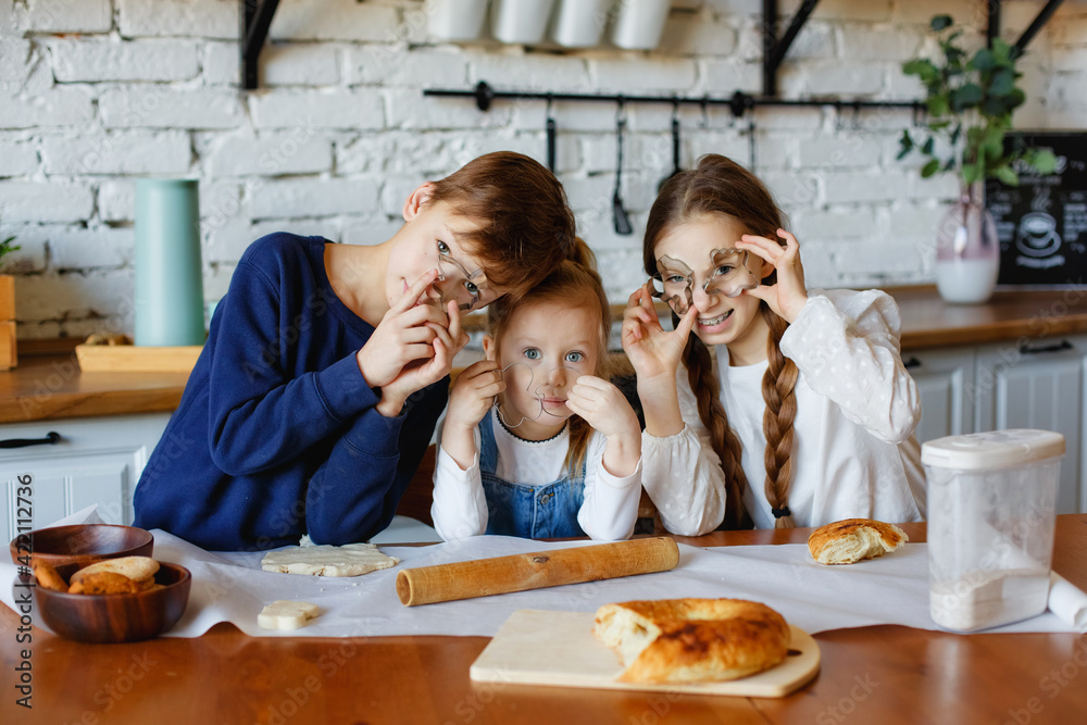 Three children stand holding cookie molds to their faces. Have fun in the kitchen. Prepare cookies for parents. Three children stand holding cookie molds to their faces. Have fun in the kitchen. Prepare cookies for parents.