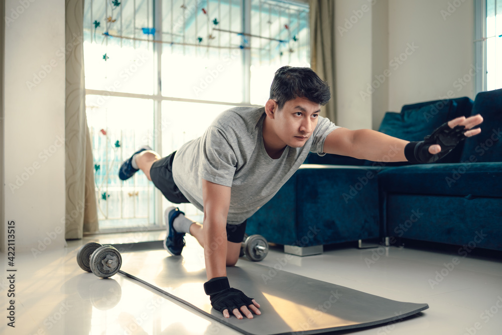 Fototapeta premium Young man making abdominal exercises on yoga mat in living room at home. Fitness, workout and traning at home concept.