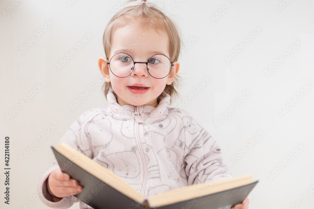 Cute toddler girl in glasses reading book on white background. Back to school concept Cute toddler girl in glasses reading book on white background. Back to school concept