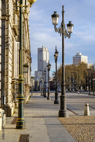 Sidewalk of the street of the Royal Palace of Madrid with street lamps and old building in sunny day. photo