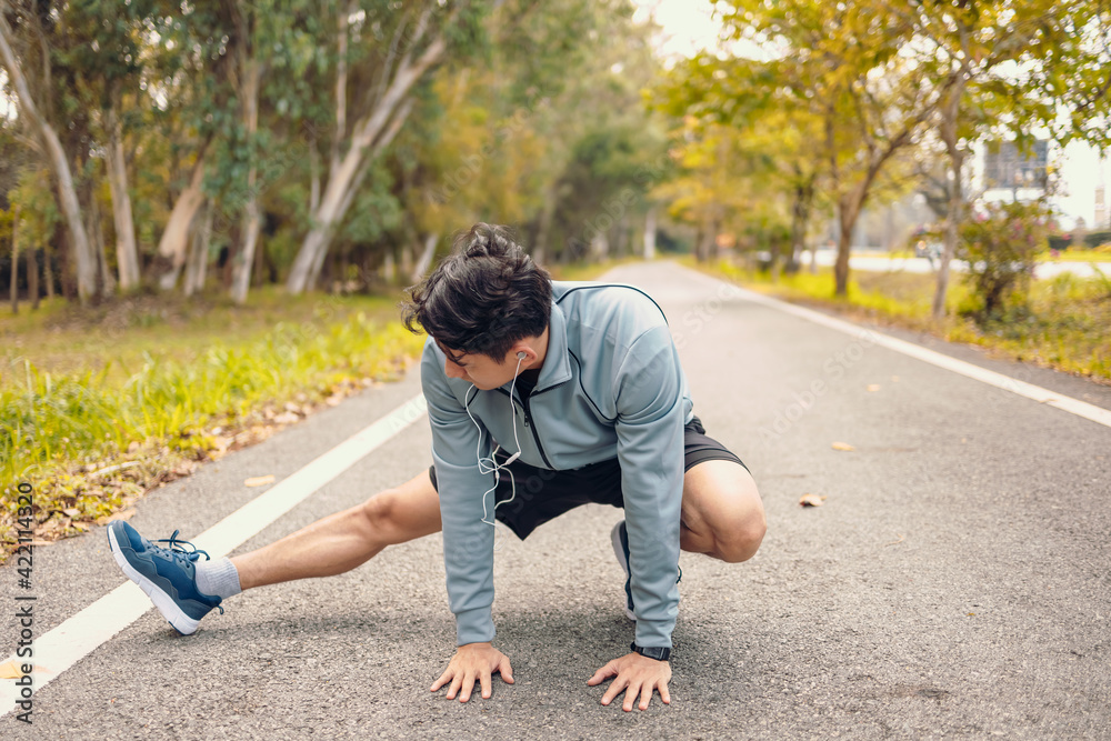 young man stretching in the park before running. Young man workout before fitness training at the park. Healthy and exercise young man warming up on the road beside the forest. young man stretching in the park before running. Young man workout before fitness training at the park. Healthy and exercise young man warming up on the road beside the forest.