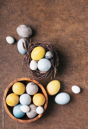 Bright easter eggs painted with natural dyes lie in a nest on a brown background, copy space, flat lay