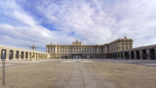 Esplanade and large courtyard of the royal palace of Madrid at sunrise on a day with blue sky and clouds.