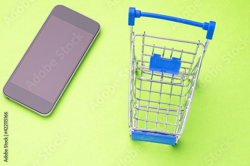 modern smartphone and shopping cart on a colored background