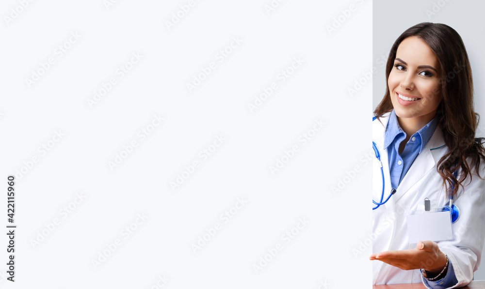Portrait of happy smiling female doctor showing empty signboard with copy space empty area for some text, over grey. Young brunette beautiful woman in medical, clinic, healthcare studio concept. Portrait of happy smiling female doctor showing empty signboard with copy space empty area for some text, over grey. Young brunette beautiful woman in medical, clinic, healthcare studio concept.