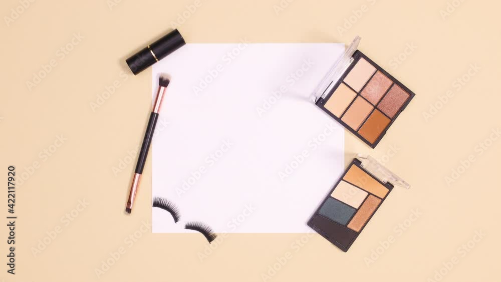 Make up products and blinking eye lashes appear around paper card note. Stop motion flat lay Make up products and blinking eye lashes appear around paper card note. Stop motion flat lay