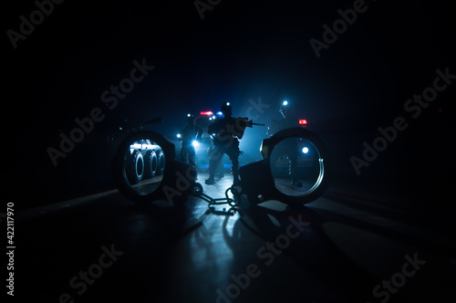 Police raid at night and you are under arrest concept. Silhouette of handcuffs with police car on backside. Image with the flashing red and blue police lights at foggy background.