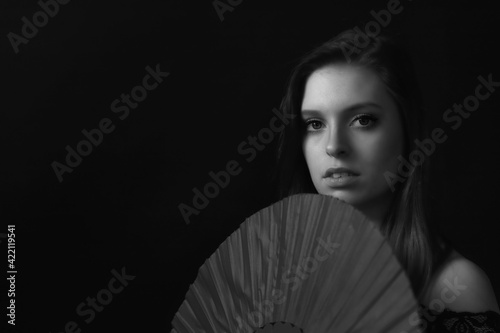 Low key black and white portrait of beautiful young woman holding the fan. Horizontally. 