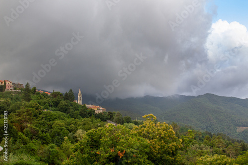 The bell tower of the temple is surrounded by dense vegetation against the backdrop of mountains, low clouds, bright sunlight after rain.