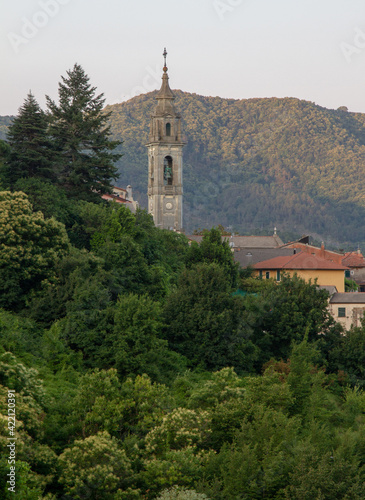 The bell tower of the temple is surrounded by houses and dense vegetation against the backdrop of mountains.