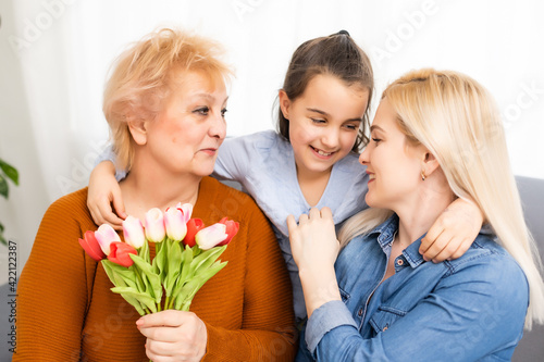 A little girl gives a bouquet of tulips to her mom and grandmother. They celebrate Mother's Day. They have a traditional family holiday.