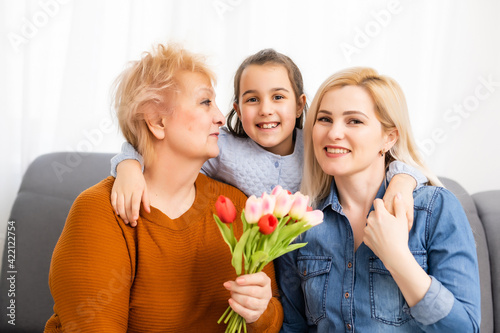 Photo portrait of granddaughter congratulating granny giving tulips bunch sitting near mom