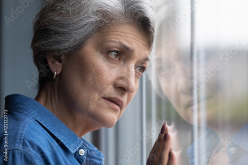 Solitude hurts so much. Cropped shot of lonely older hispanic lady lean head to window glass look at distance feel abandoned grief suffer alone. Depressed elderly woman widow mourning for gone husband