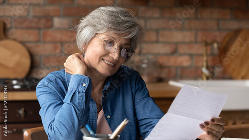 It seems interesting. Focused elderly latin woman engaged in reading commercial offer in letter from bank think on good loan terms conditions. Concentrated old lady in glasses do paperwork check bills photo