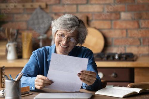 Happy retired hispanic woman bank client hold official document notification informing loan mortgage is paid. Glad smiling aged latin lady read paper letter received by mail satisfied with good news