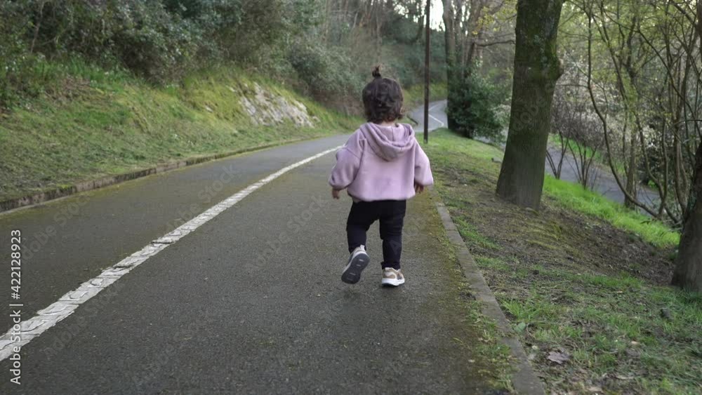 Back view of toddler running, then laughing looking at camera. Tracking shot