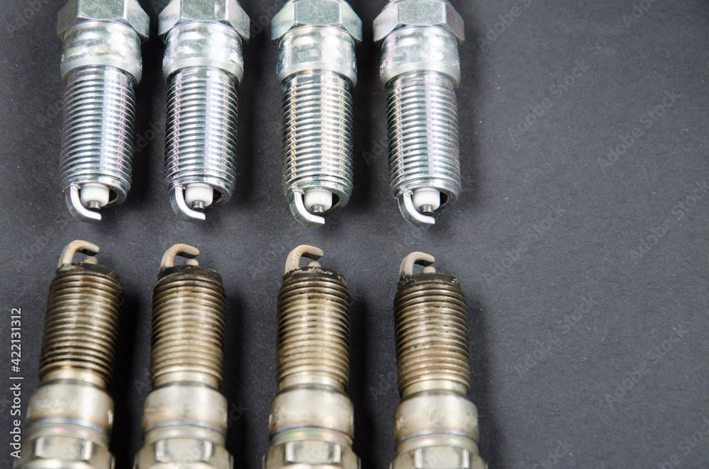Four new car spark plugs lie in a row on a gray background..Opposite them are four old worn spark plugs..Result before and after..Car parts..Car maintenance. Four new car spark plugs lie in a row on a gray background..Opposite them are four old worn spark plugs..Result before and after..Car parts..Car maintenance.
