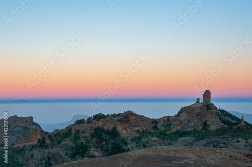 Roque Nublo, symbolic natural monument of Gran Canaria in sunset evening light. Red and orange sunset and sea in background. Emblematic volcanic rock formations in mountains of Gran Canaria Spain.