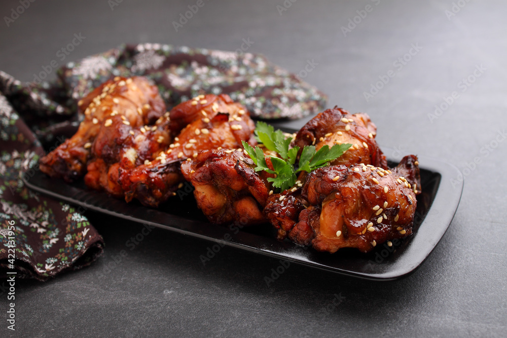 Plate of chicken wings in soy sauce with honey and sesame. Traditional asian recipe. Dark background.