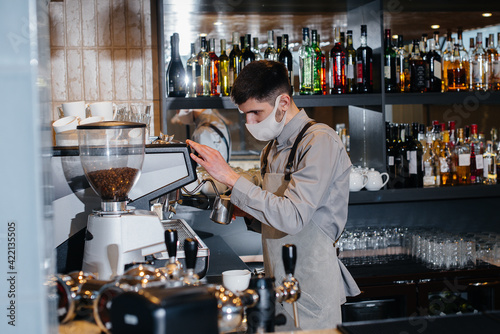 A masked barista prepares delicious coffee at the bar in a cafe. The work of restaurants and cafes during the pandemic.