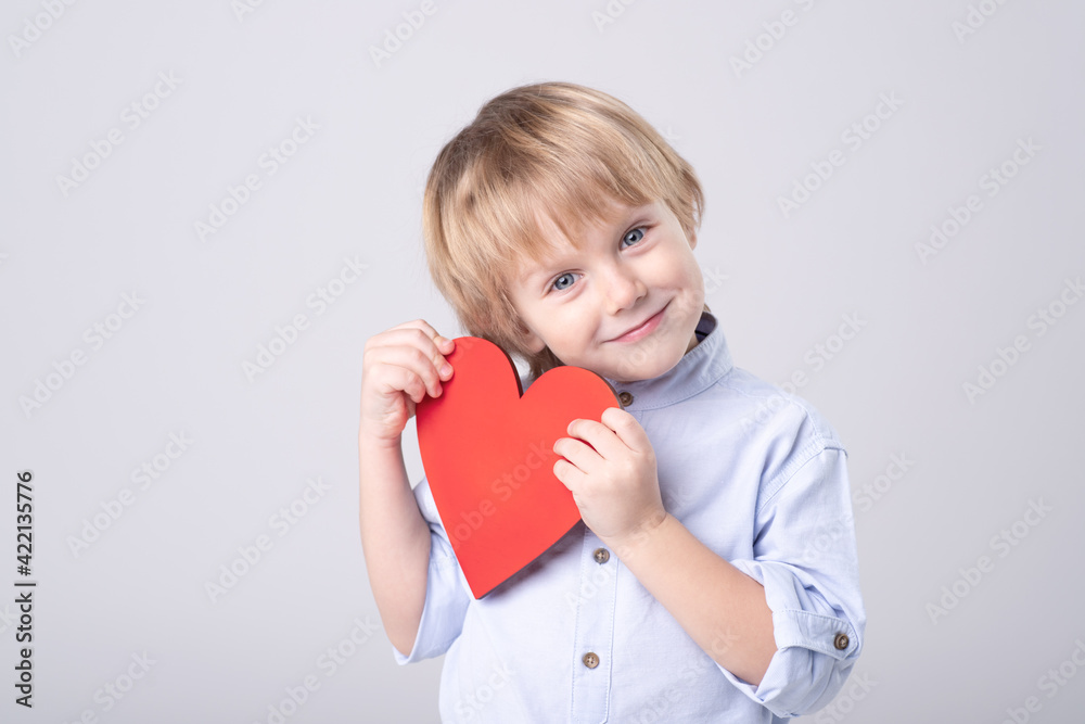 Cute Caucasian child is tenderly holding toy red heart on white background. Eye contact. Studio light. Concept of childhood, love, mother's day, health care, valentine. Horizontal. Copy space. Cute Caucasian child is tenderly holding toy red heart on white background. Eye contact. Studio light. Concept of childhood, love, mother's day, health care, valentine. Horizontal. Copy space.
