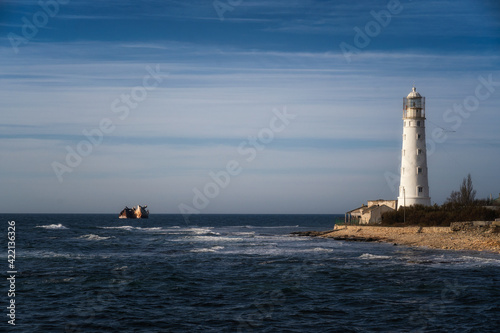Lone beacon guards the ships. The lighthouse shows the way for boats. Wrecked ship lays nearby © Biskariot