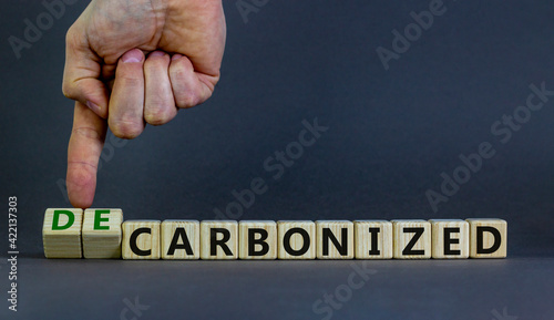 Carbonized or decarbonized symbol. Businessman turns wooden cubes and changes words 'carbonized' to 'decarbonized'. Grey background, copy space. Business, Carbonized or decarbonized concept. photo