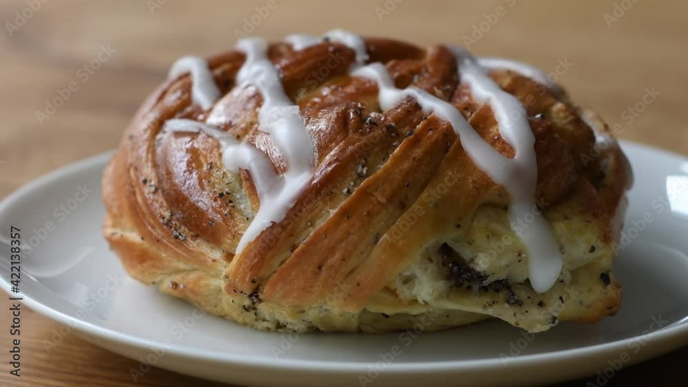 Hand adding a big cinnamon bun with icing to the white plate on the wooden table. Footage made in Sweden. Hand adding a big cinnamon bun with icing to the white plate on the wooden table. Footage made in Sweden.