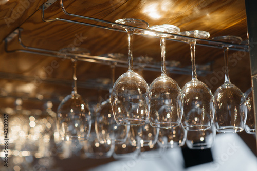 Clean glasses for alcoholic beverages hang over the bar in a modern restaurant. © Andrii