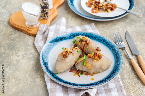 Traditional Lithuanian dish Zeppelin, boiled potato dumplings stuffed with minced pork, on a colored ceramic plate on a gray concrete background.