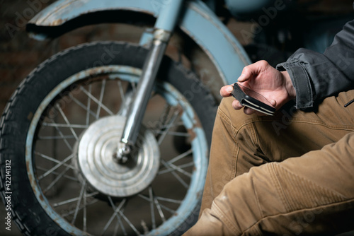 A motorbiker is sitting with a mobile phone in hands close up.