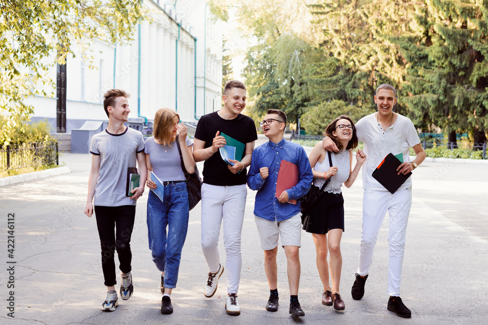 Group of friends walking home after classes. Young boys and girls having a good time in students campus on a warm sunny spring day.