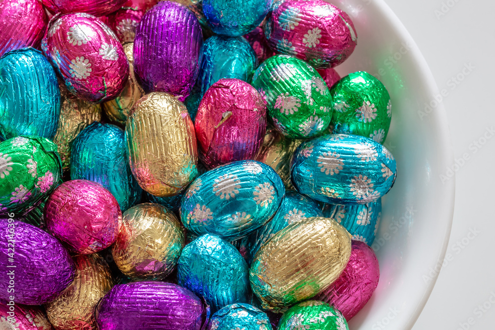 White bowl full of Chocolate Candy eggs in colorful foil for Easter White bowl full of Chocolate Candy eggs in colorful foil for Easter