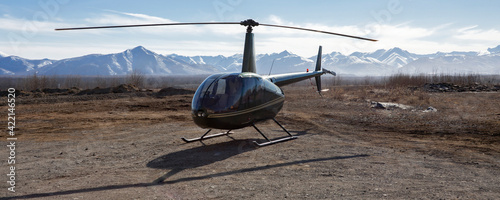 Small helicopter is parked on a dirt platform against the backdrop of mountains.
