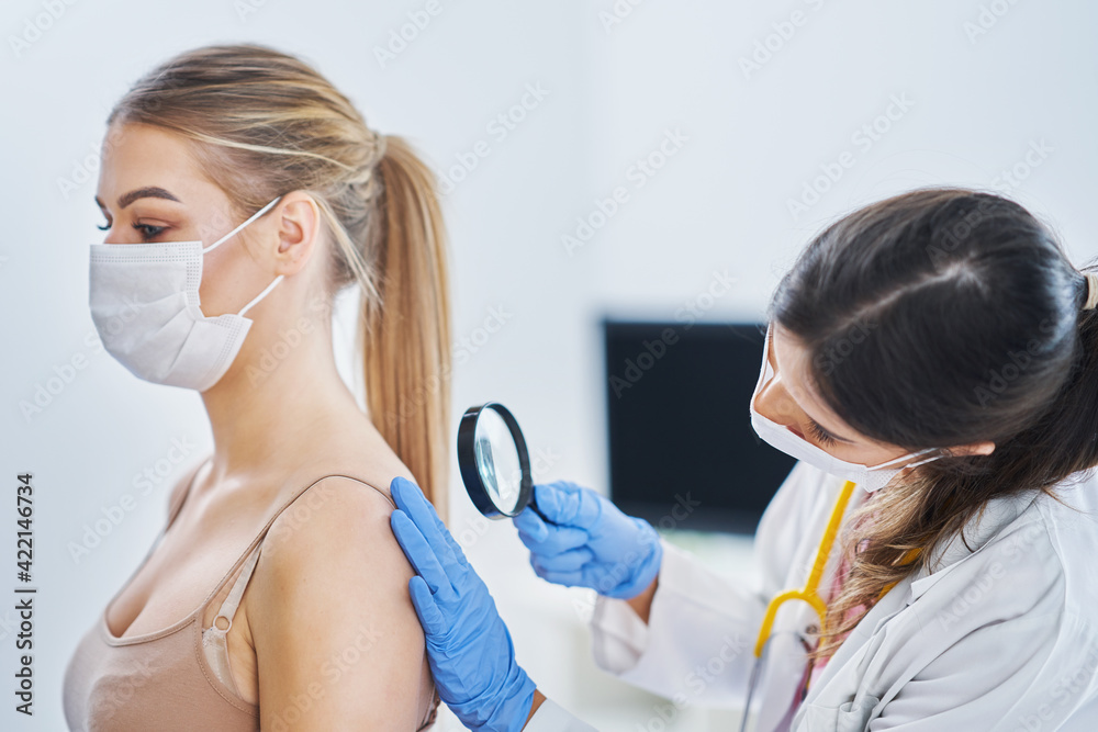 Dermatologist in mask checking up on her female patient Dermatologist in mask checking up on her female patient