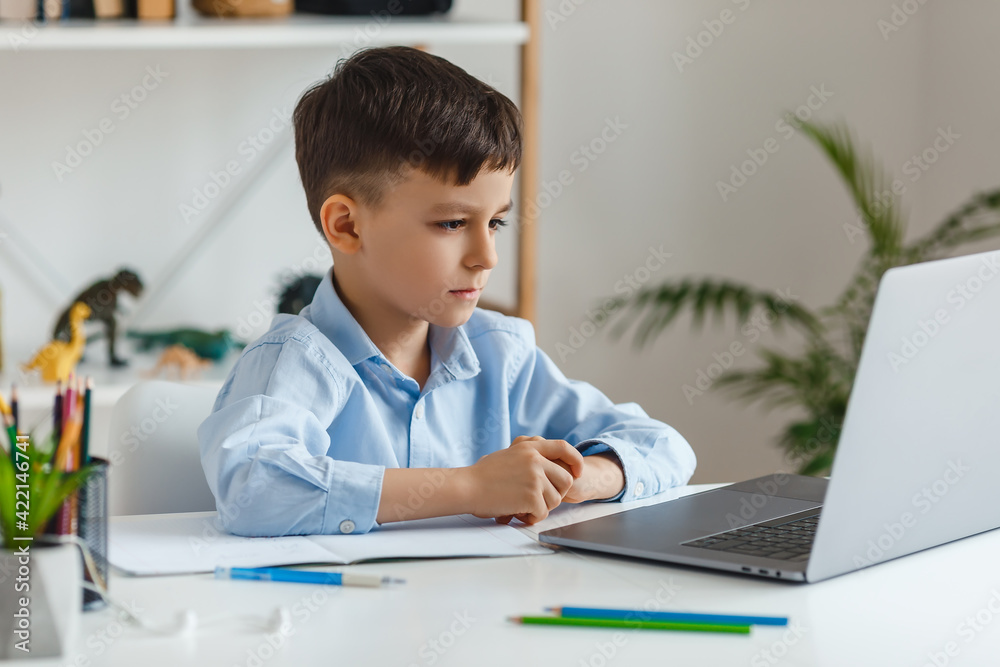 Clever kid doing homework using laptop and internet. Elementary school e-learning via video call. Boy studying online at home Clever kid doing homework using laptop and internet. Elementary school e-learning via video call. Boy studying online at home