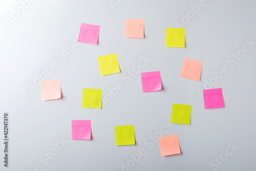 Empty paper stickers of pastel shades hang on light wall. Front view of chaotically arranged notes.