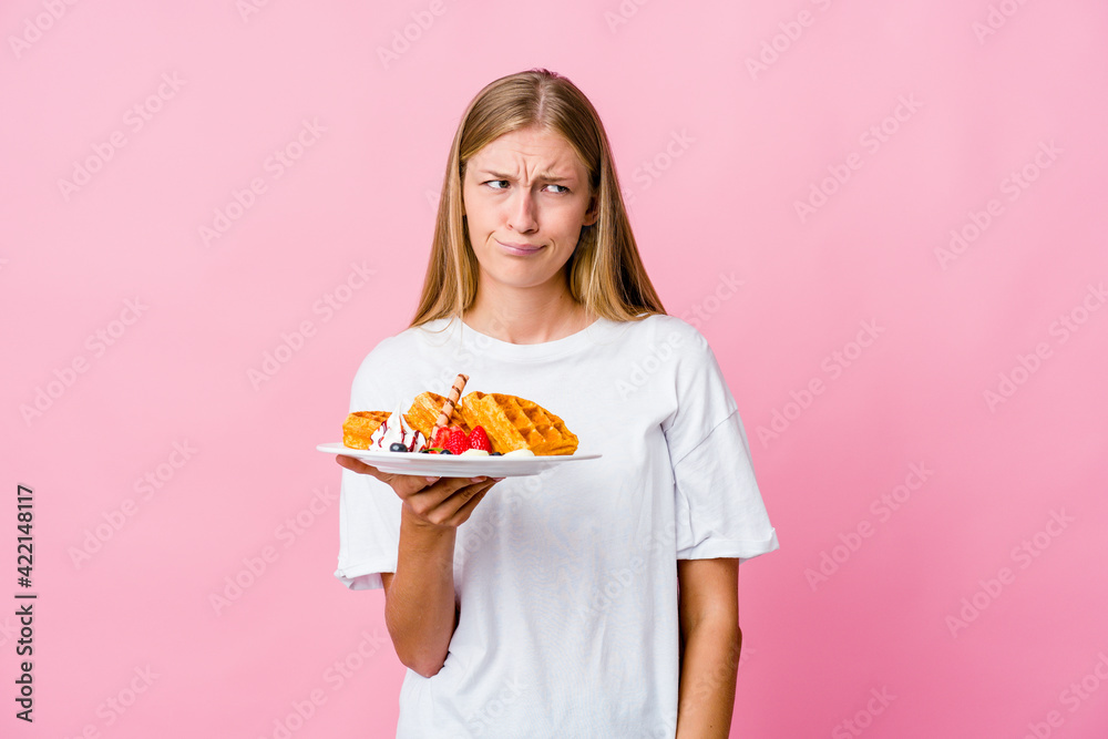 Young russian woman eating a waffle isolated confused, feels doubtful and unsure. Young russian woman eating a waffle isolated confused, feels doubtful and unsure.