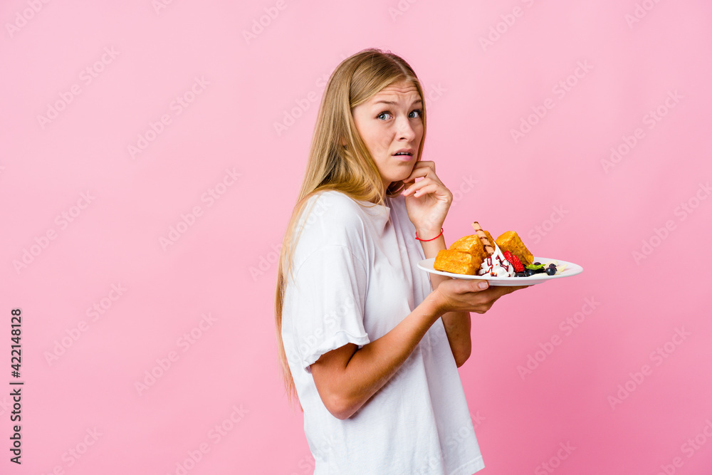 Young russian woman eating a waffle isolated scared and afraid. Young russian woman eating a waffle isolated scared and afraid.
