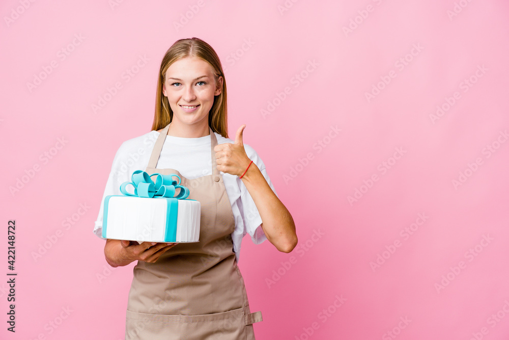 Young russian baker woman holding a delicious cake smiling and raising thumb up